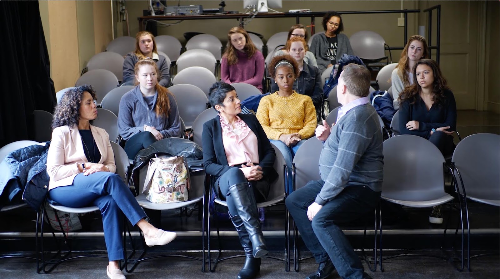 A number of students in stadium-like seating talking with professors.