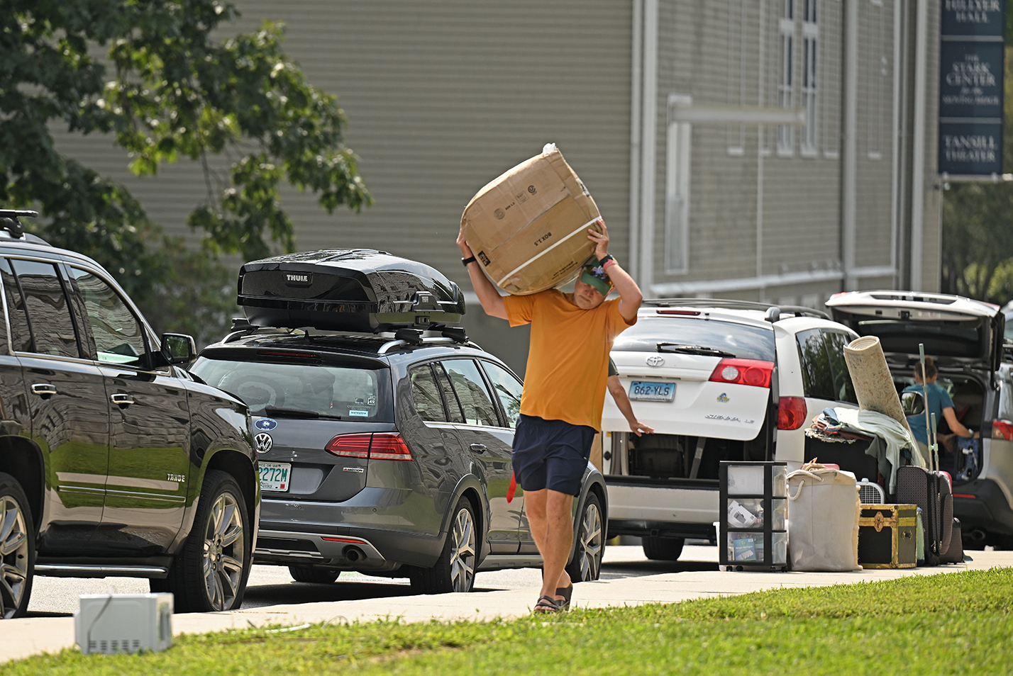 A man carries a large box along a line of cars on college move in day.