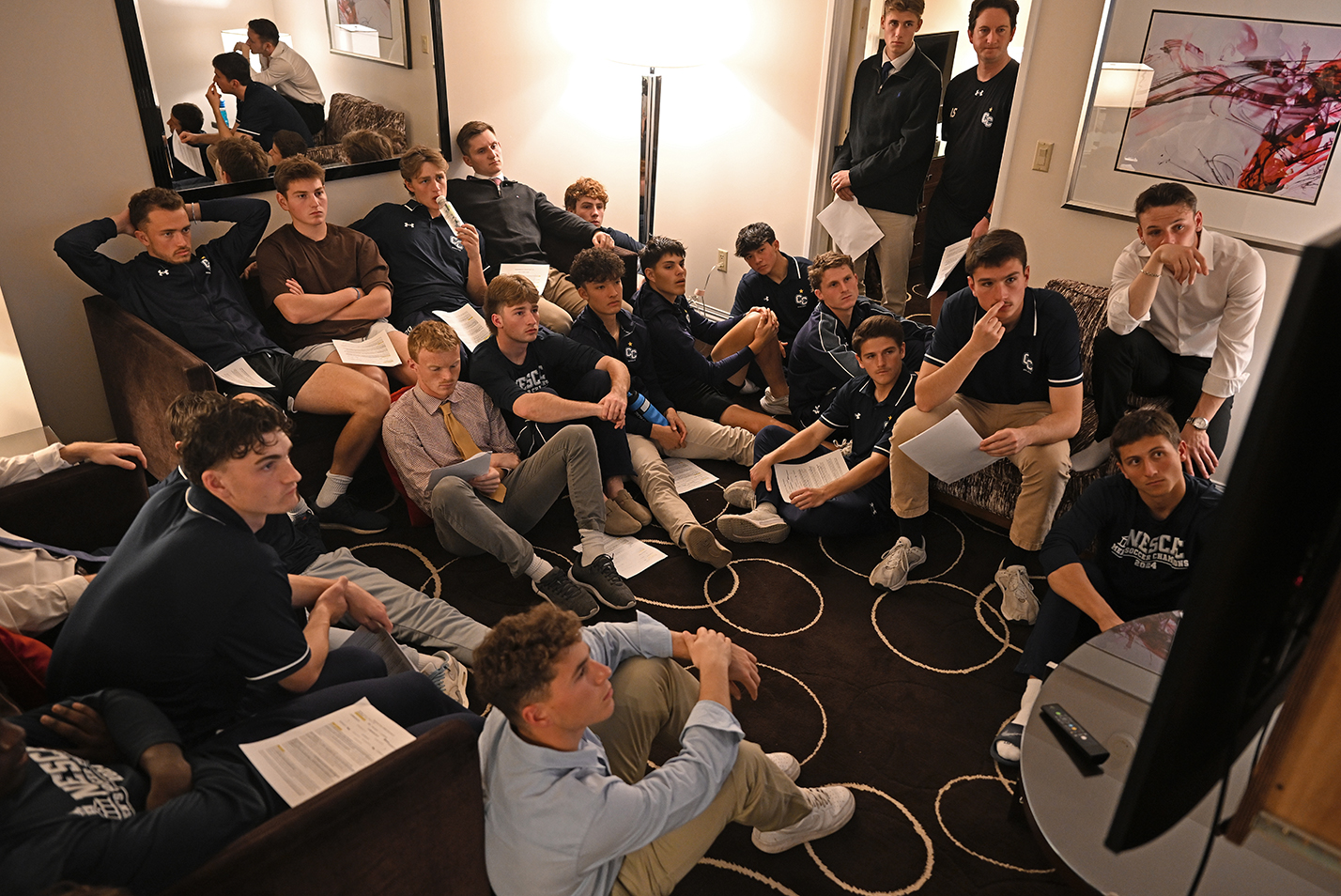 A soccer team crowds into a hotel suite to watch game film and scout their opponent.