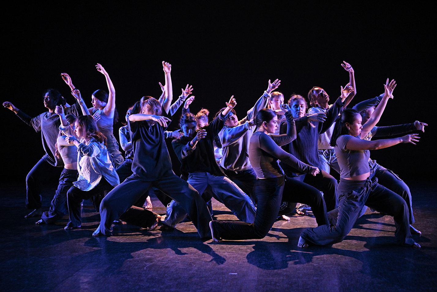 A large group of dancers perform with dramatic gestures on stage.