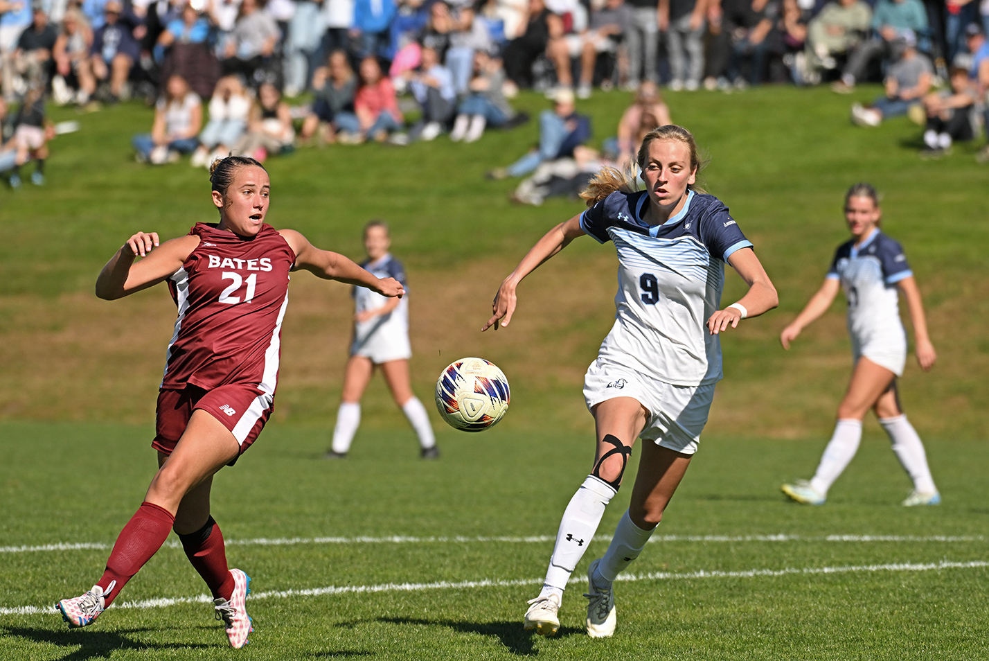 Soccer players pursue a ball across the pitch.