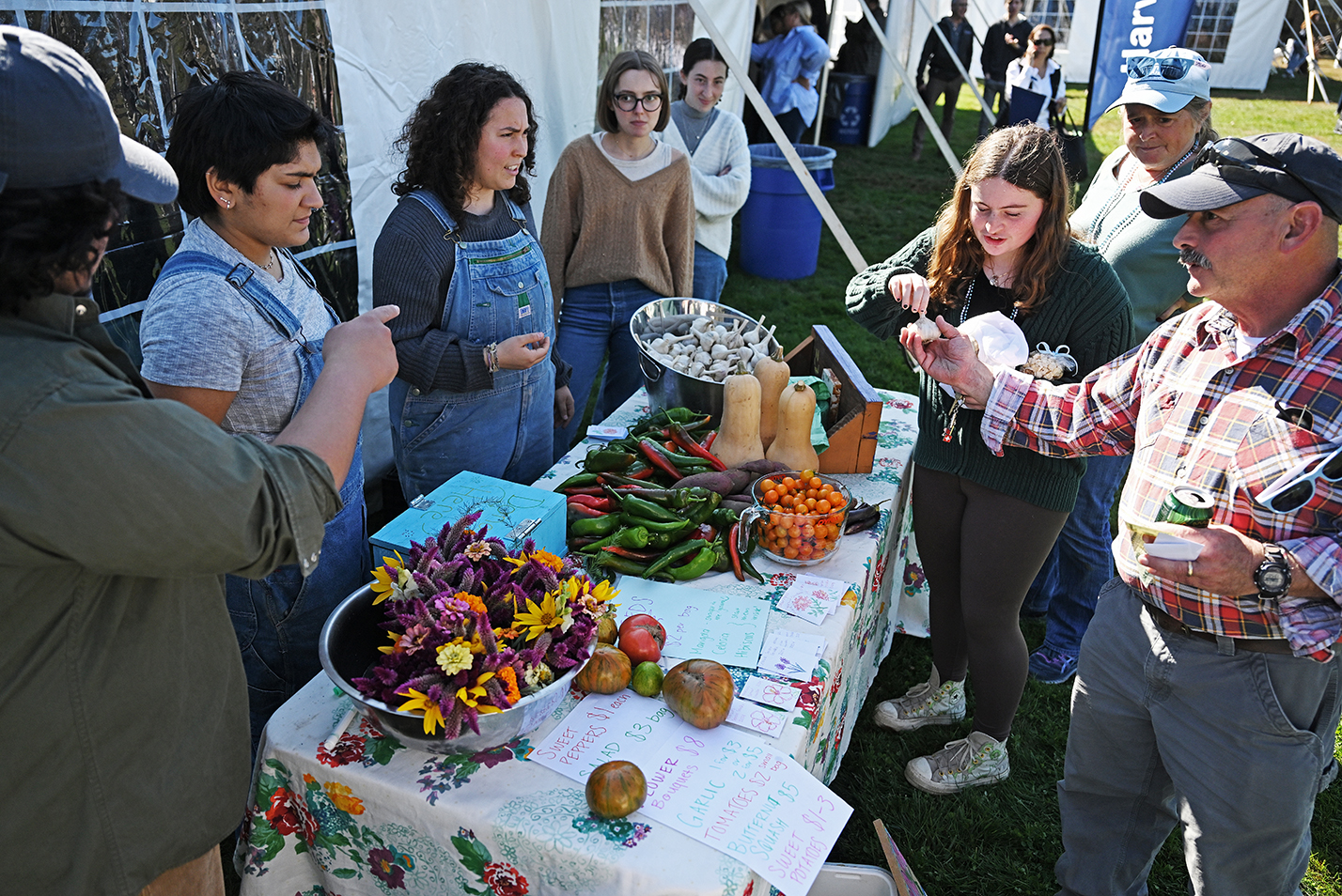 A group of people gather around a farmer's market table.