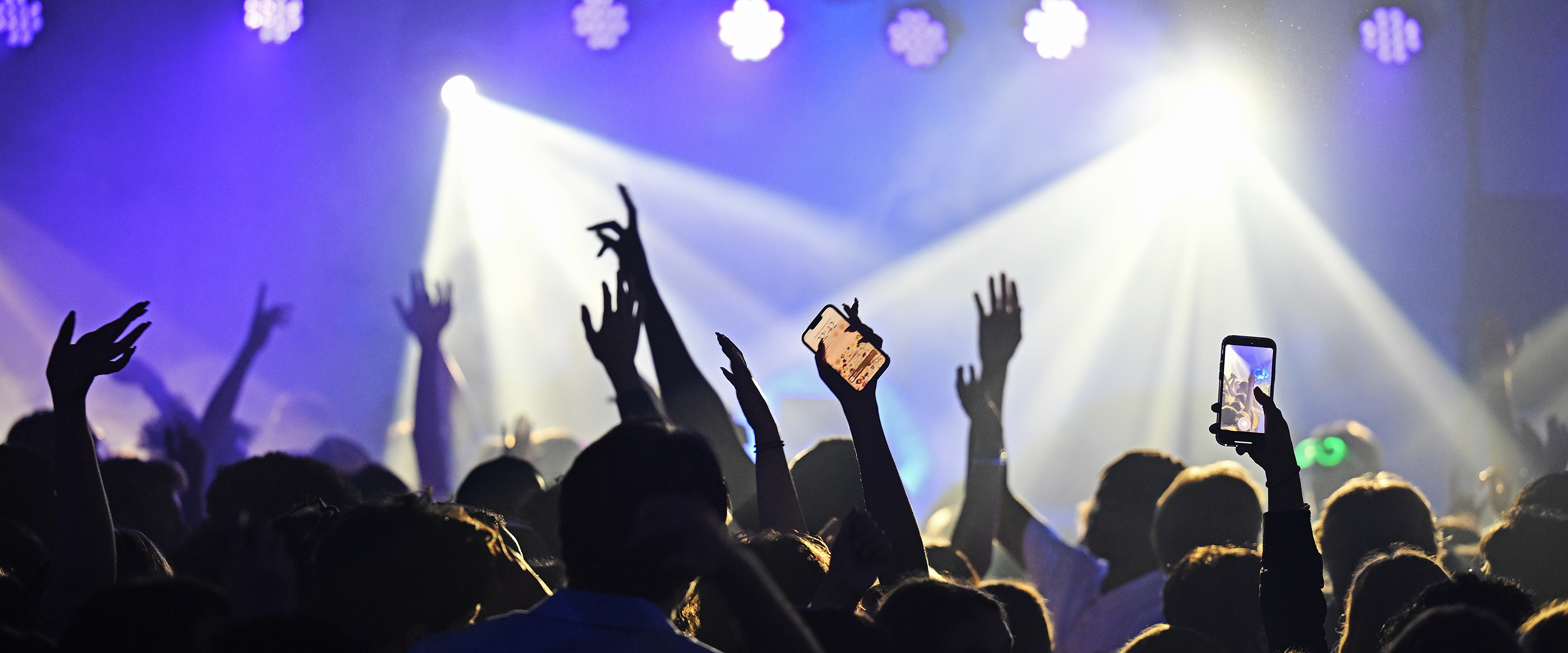 students, arms raised, dance in the flashing lights from a DJ on stage