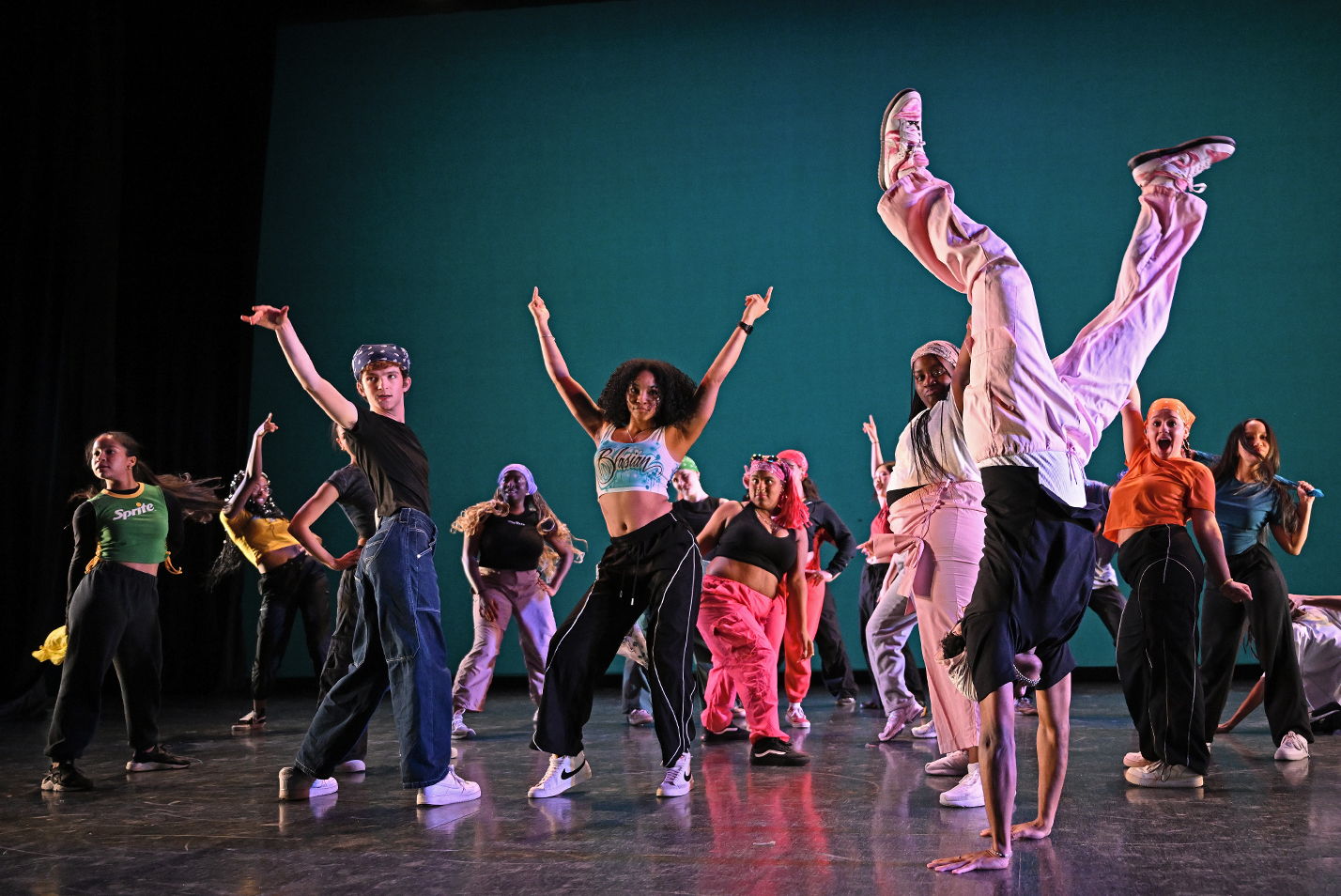 A group of dance students, clad in a variety of colorful costumes, perform a hip hop dance.